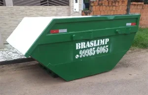 imagem de uma caçamba papa entulho estacionada em uma rua sem asfalto, em frente a 2 imóveis, um com tijolos sem embolso e outro com lajotas cinzas